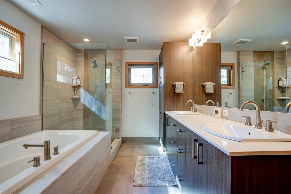 A modern, spa-inspired bathroom featuring a freestanding soaking tub, glass-enclosed walk-in shower, double vanity sinks with large mirrors, and abundant natural light. The space is designed for relaxation and rejuvenation, echoing upscale spa environments.