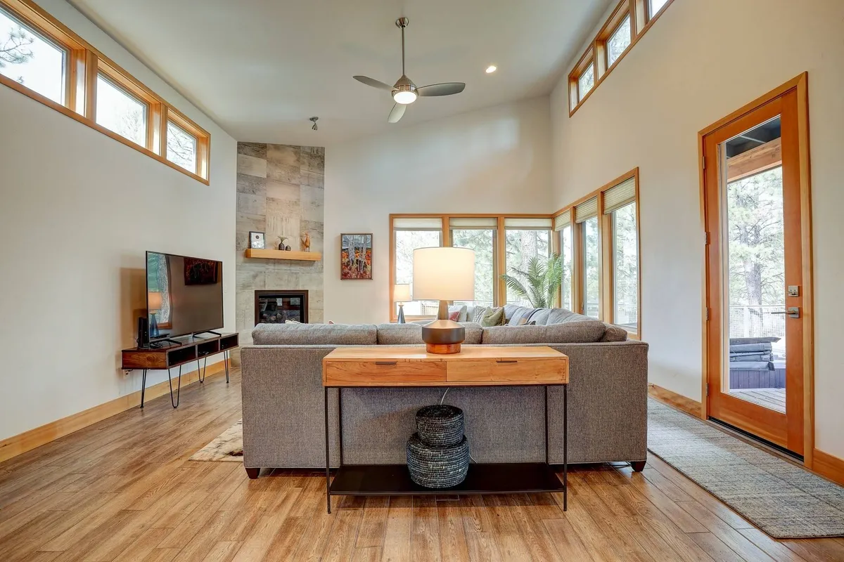 A warm, inviting living space featuring a plush sofa, coffee table, television, cozy fireplace, and large sunlit windows. The arrangement encourages groups to relax, socialize, or unwind together after a day spent outdoors.