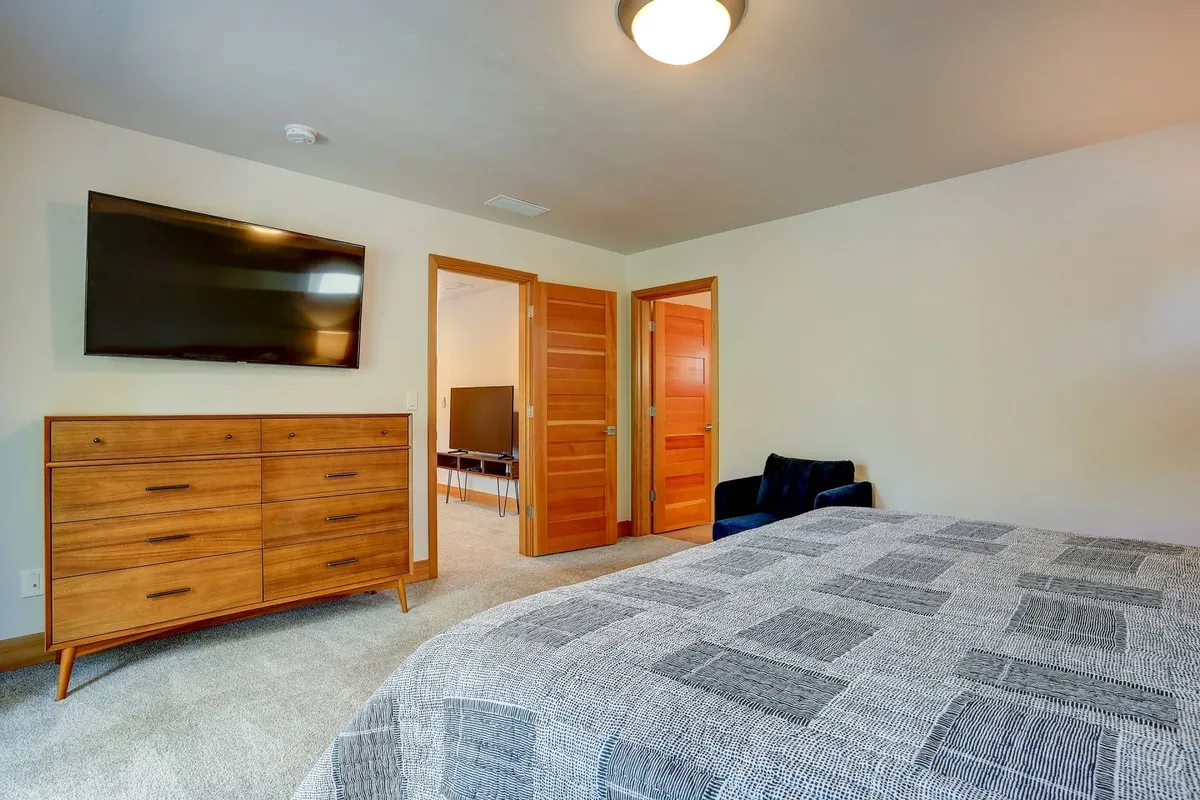 A comfortable upstairs lounge area with a bed, dresser, television, and double doors letting in gentle daylight. The setup suggests flexibility—ideal for afternoon naps, extra guests, or winding down with a favorite show.