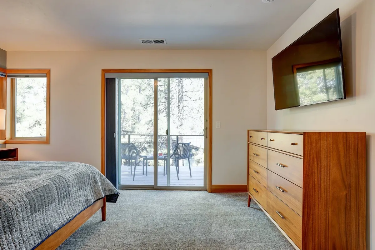 A tranquil bedroom scene featuring a cozy bed, dresser, and sliding glass door that opens to serene nature views. This inviting space bathes in natural light, suggesting peaceful mornings and restful evenings—an ideal setting for couples.