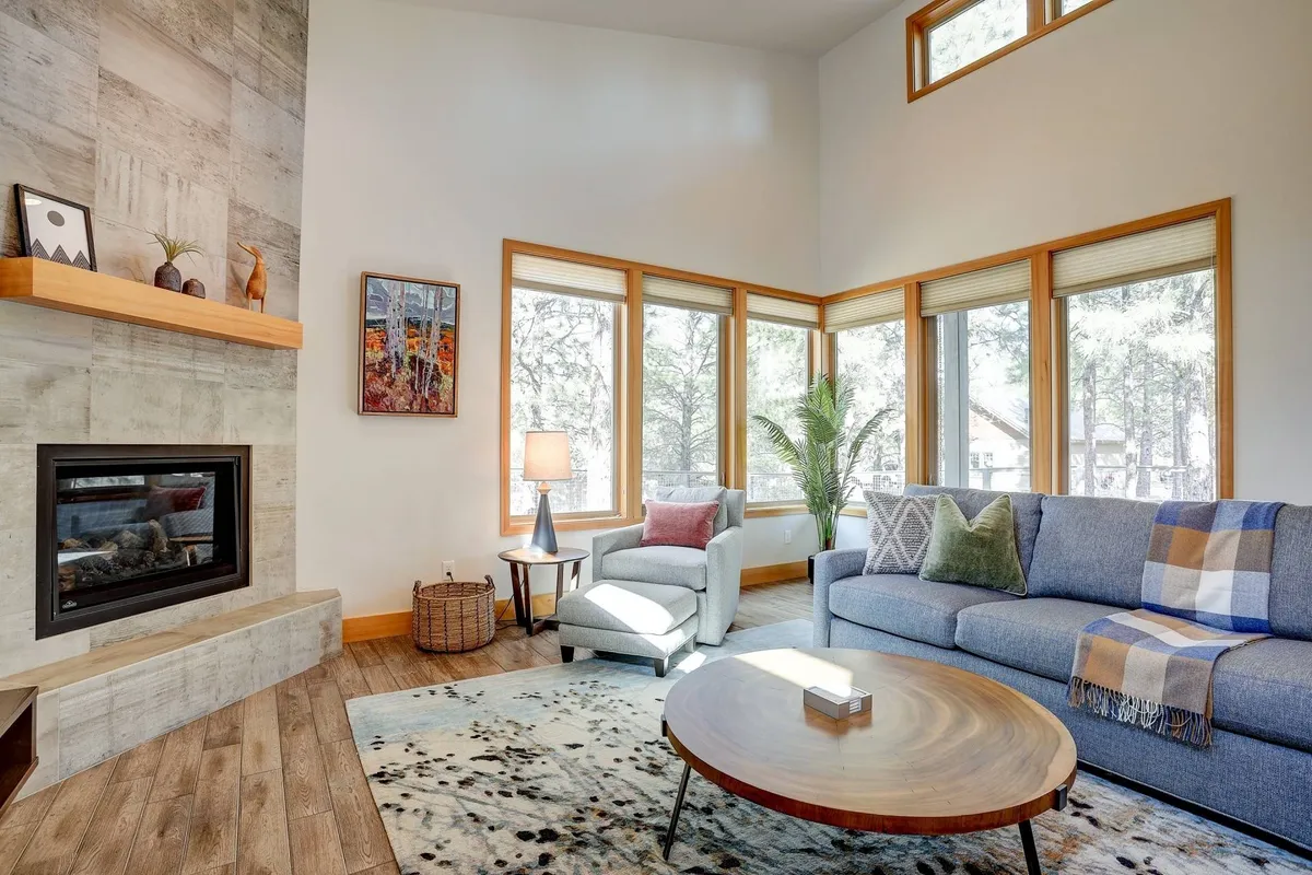 A stylish and cozy living space anchored by a modern fireplace, flanked by large windows that bring in ample sunlight. The sofa and coffee table offer a comfortable setting for conversation or reading, while decorative touches add a warm, artistic flair.