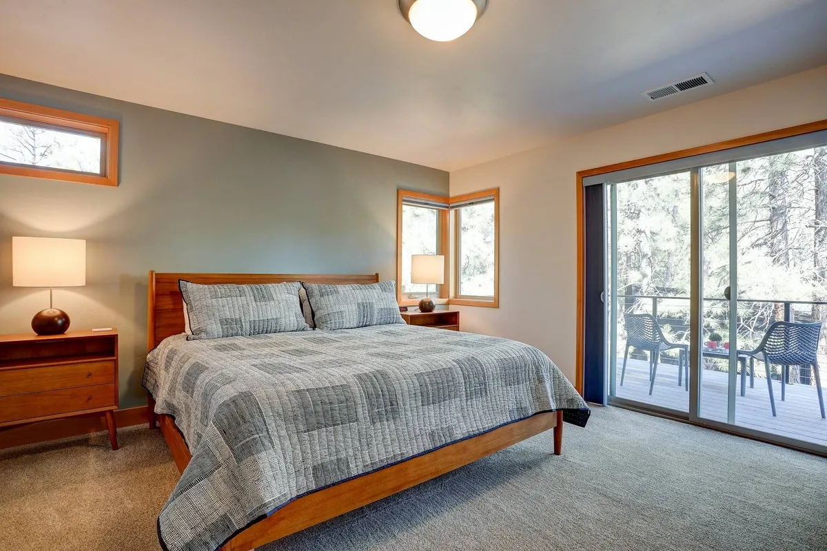 A serene bedroom with a neatly made bed, a window offering gentle natural light and views of the outdoors, a nightstand with a lamp, and inviting space for morning coffee or reading. The tranquil mood and elegant setup evoke restful comfort, aligning with the concept of a master suite retreat.