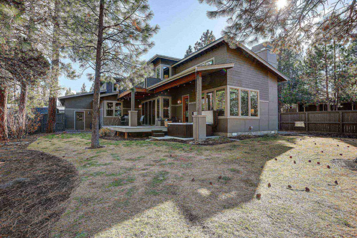 A spacious deck bordered by tall trees with large windows reflecting greenery, inviting guests to relax and gather outdoors in the fresh mountain air. The tranquil setting is ideal for unwinding after a day of adventure.